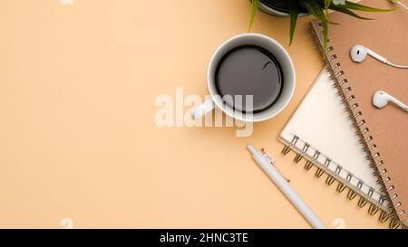A simple workspace with black coffee cup, notebooks, pen, earphone, plant and copy space for product display on beige background. top view Stock Photo