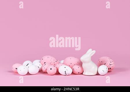White and pink Easter eggs with small bunny sculpture on pink background with copy space Stock Photo