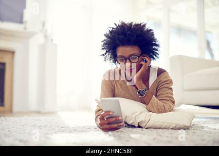 Scrolling through to get to the good stuff. Shot of a young woman using her phone at home. Stock Photo