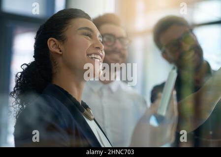Brainstorming theyre way to success. Shot of a group of colleagues brainstorming together on a glass wall in an office. Stock Photo