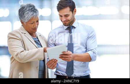 Reviewing the numbers. Shot of two business colleagues discussing work while standing with a digital tablet. Stock Photo