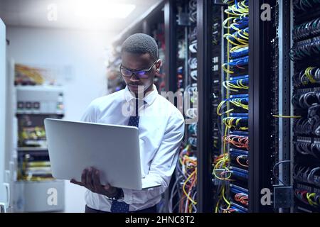 The man with the plan. Cropped shot of a IT technician working on his laptop while standing inside of a server room. Stock Photo