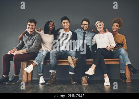 Colleagues that have become friends. Studio shot of a diverse group of creative employees embracing each other against a grey background. Stock Photo