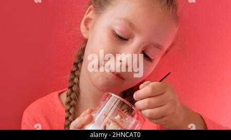 Child eating yogurt jelly pink background. Dairy product diet Lactobacillus Acidophilus, healthy homemade breakfast menu. Kids healthcare. Vegan food Stock Photo