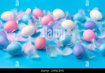Easter background with colored eggs and feathers on a blue background. Side view. Stock Photo