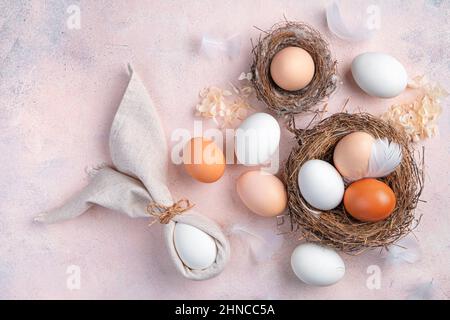Easter bunny made of napkins and eggs in a nest on a light pink background. The concept of a Happy Easter. Top view. Stock Photo