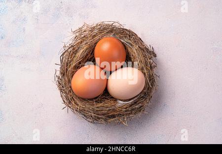 A nest with chicken eggs on a light pink background. Top view, close-up. The concept of Easter. Stock Photo