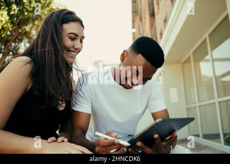 Biracial romantic couple laughing while scrolling on digital tablet  Stock Photo