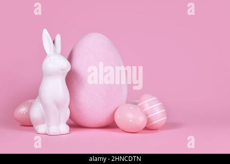 White bunny sculpture with easter eggs on pink background with copy space Stock Photo