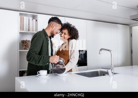 happy african american man pouring coffee near cheerful pregnant wife Stock Photo