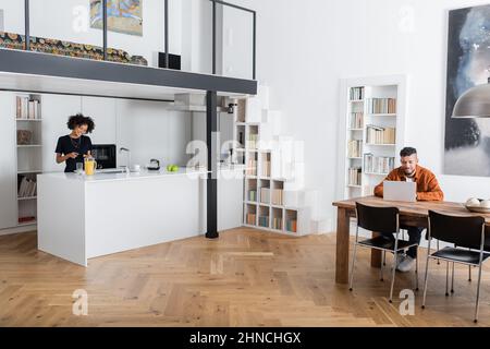 cheerful african american woman making sandwich while boyfriend working from home Stock Photo