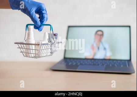 urchase of medicines using the computer application for home delivery. Pharmacist on laptop screen. A hand in a rubber glove puts on the table a Stock Photo