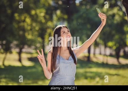 Photo of adorable brown hair girl take selfie portrait on telephone show v-sign enjoying summer weekends vacation walk outside in park Stock Photo
