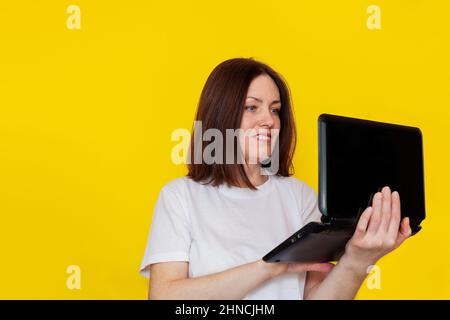 Portrait of a woman in a white t-shirt with a laptop on a yellow background. Business woman working with laptop at home. The concept of remote work Stock Photo