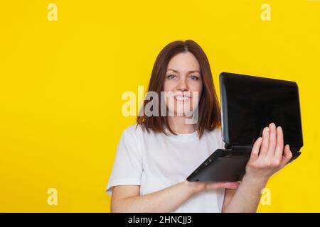Portrait of a woman in a white t-shirt with a laptop on a yellow background. Business woman working with laptop at home. The concept of remote work or Stock Photo