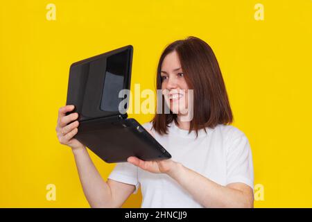 Portrait of a woman in a white t-shirt with a laptop on a yellow background. Business woman working with laptop at home. The concept of remote work or Stock Photo
