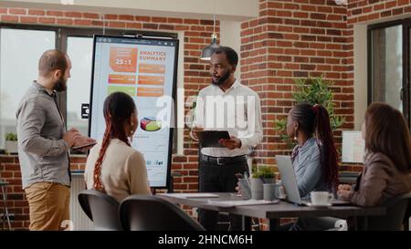 Diverse people presenting business project and strategy in meeting office. Workmates doing financial presentation on monitor in front of colleagues, working on development and growth. Stock Photo