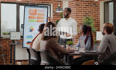 Company employee presenting business strategy with charts on monitor, planning project. Workmates analyzing financial statistics on display, working together on company development. Stock Photo