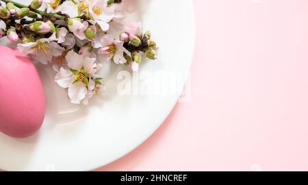 Easter table decoration, almond blossoms and Easter eggs on a white plate, pink color background, copy space. Stock Photo