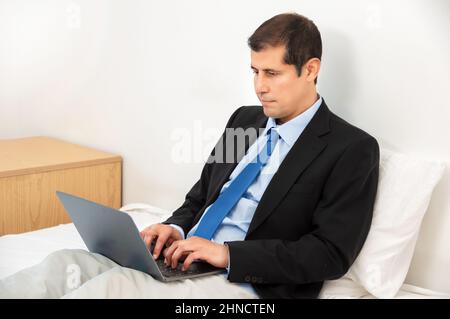 Mature business man holding a cup of coffee and working with laptop on bed Stock Photo