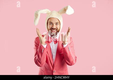 Positive funny man in soft white hat with ears of rabbit who is sincerely happy on pink background. Stock Photo