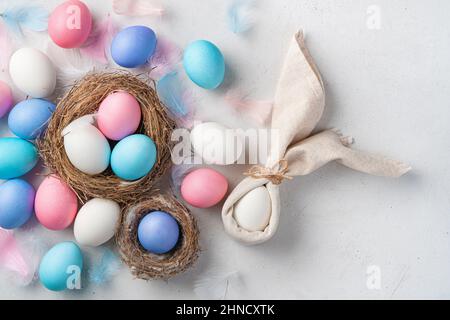 Easter background with a rabbit from a napkin and colored eggs on a gray background. Top view, copy space. Stock Photo