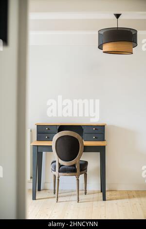 Comfortable chair at classic black secretary desk placed at white wall in light room with round chandelier in spacious apartment Stock Photo