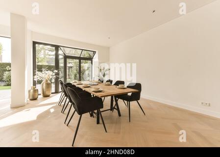 Chairs at wooden table with dinnerware placed in dining room near kitchen zone in spacious apartment with flowers in vase Stock Photo