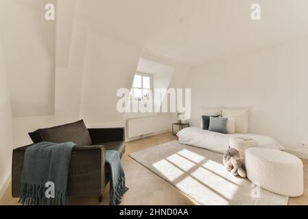 Interior of modern room in house furnished with comfortable sofa and bed and settee with cushions near poufs and plush toy on carpet Stock Photo