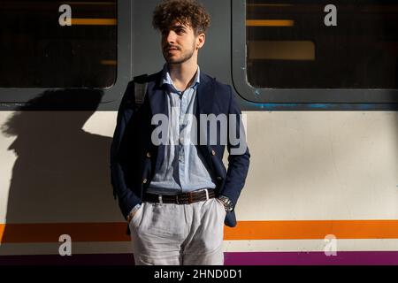 Handsome bearded Hispanic male looking away and standing near train while waiting for departure on platform on sunny summer day Stock Photo