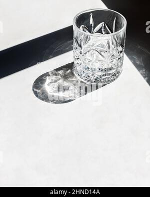 From above empty lowball glass placed on white table near shadow and reflecting bright sunlight in daytime Stock Photo