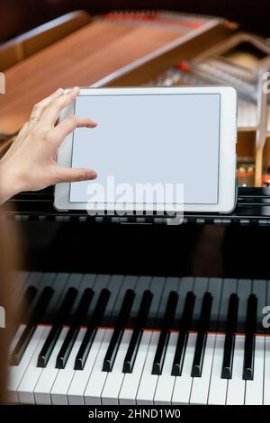Crop female musician touching tablet with blank screen while sitting at piano and studying in music school Stock Photo