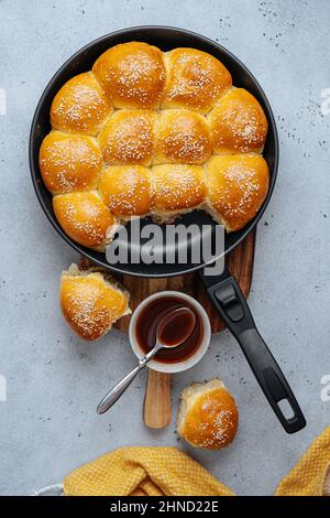 From above of tasty pull apart bread rolls with sesame seeds in frying pan served on wooden cutting board with sweet sauce Stock Photo