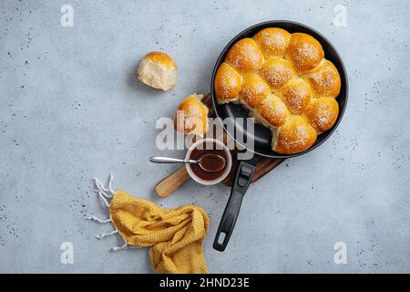 From above of tasty pull apart bread rolls with sesame seeds in frying pan served on wooden cutting board with sweet sauce Stock Photo