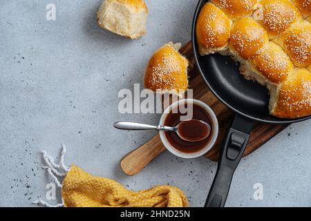 From above of tasty pull apart bread rolls with sesame seeds in frying pan served on wooden cutting board with sweet sauce Stock Photo