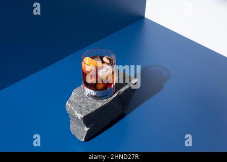 from above glass of alcoholic cocktail made with red vermouth served with orange slices on stone in light studio with blue and white wall Stock Photo