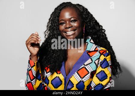 Happy African American Woman with curly hair smiling at camera while standing against white wall Stock Photo