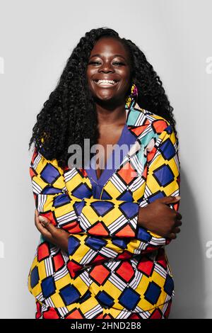 Happy African American Woman with curly hair in stylish outfit smiling and looking at camera while standing on white background Stock Photo
