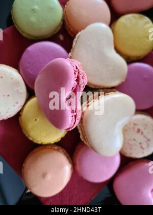 Top view of three delicious macarons and love heart symbol on napkin on wooden table. Romantic vintage valentines day and wedding background Stock Photo