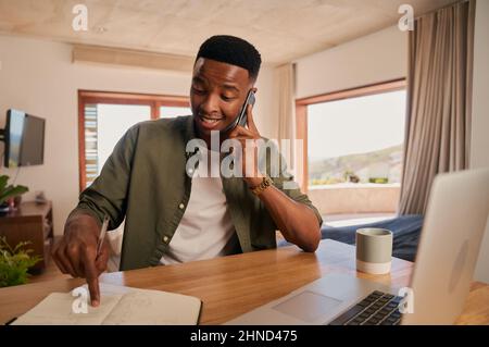 Young adult black male surprised while talking on the phone to colleague. Happy working from modern home remotely. Stock Photo