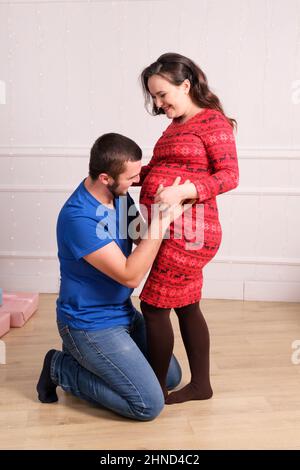 Happy future parents are expecting the birth of a baby, the husband strokes the belly of his pregnant wife, vertical photo. Stock Photo