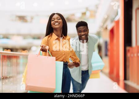 Excited Black Woman Pulling Man To Shopping Store Stock Photo