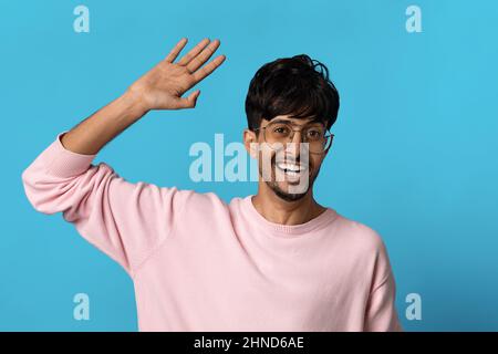 Positive middle eastern guy waving at camera on blue Stock Photo