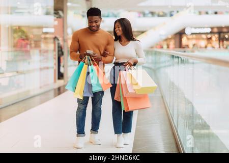 Happy black couple using phone walking with shopping bags Stock Photo