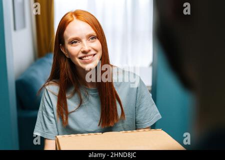 Close-up face of happy young woman receiving paper boxes with hot pizza from delivery man on doorstep at home. Stock Photo