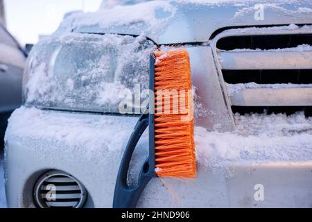 car brush-scraper for cleaning the car from snow and ice on the background of a snow-covered car. Cleaning car windows and headlights from snow with a Stock Photo