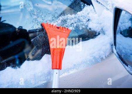 car scraper for cleaning car windows and mirrors from snow and ice. Cleaning car windows and headlights from snow with a brush. Stock Photo