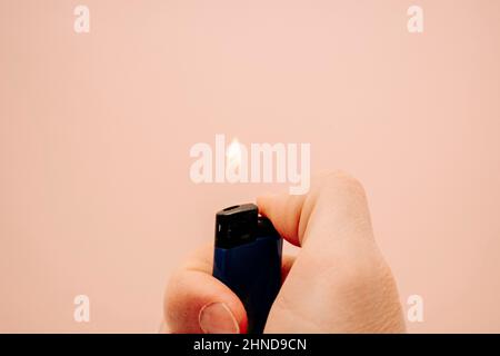 lighter with fire in hand on a peach background, copy space, control, energy, heat Stock Photo
