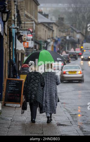 Ramsbottom, Lancashire, UK, Wednesday February 16, 2022. The start of Storm Dudley hits the North West of England on Bridge Street, Ramsbottom, Lancashire. Shppers take shelter under an umbrella as the rain starts to fall. Credit: Paul Heyes/Alamy News Live Stock Photo