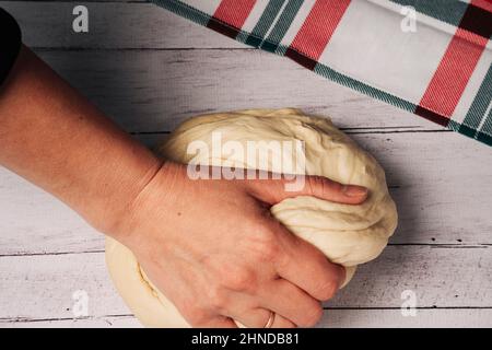 The chef's hands prepare and knead fresh homemade pizza dough on the kitchen table, Beautiful female hands knead the dough, make bread, pasta or pizza Stock Photo